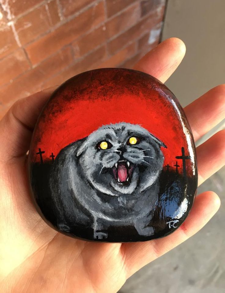 a hand holding a painted rock with a cat on it