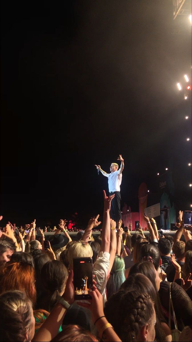 a man standing on top of his head in the middle of a crowd at a concert