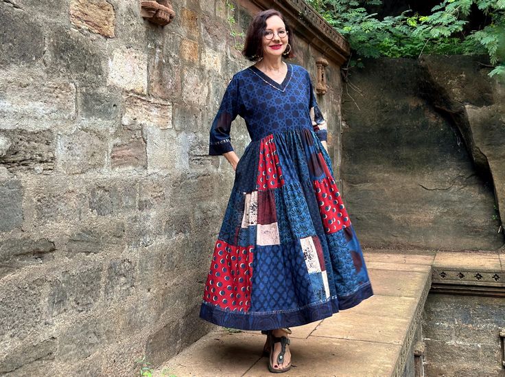 Dark indigo blue and red dress in an easy to wear Madame Hall design from hand printed, 100% cotton. It blends an international vibe with the Indian charm of superb Ajrakh block prints! The art wear vibe is unmistakable in a pattern mix of stunning fabrics, all  printed by hand with natural dyes. This dress will satisfy women who love artistry, and love India's hand handmade textiles.  It combines Ajrakh prints by one of Indias's celebrated textile artists in a Madame Hall design that'll adapt to the seasons. It'll  look just as great layered worn with boots, as it does on a sunny summer's day. I've designed this dress with a simple V neck bodice, and let loose pattern mix magic in the full tiered skirt. The pattern contrasts of gorgeous florals, polka dots and abstract are all stunning pr Traditional Cotton Dress With Natural Dye, Blue Bandhani Print Anarkali Dress, Blue Anarkali Dress With Bandhani Print, Indigo Cotton Dresses With Natural Dye, Indigo Cotton Dress With Natural Dye, Blue Bohemian Bandhani Print Dress, Red Cotton Dress With Bandhani Print, Blue Bohemian Dress With Bandhani Print, Indigo Cotton Block Print Dress