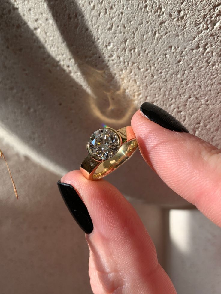 a woman's hand holding an engagement ring in front of her face and shadow on the wall