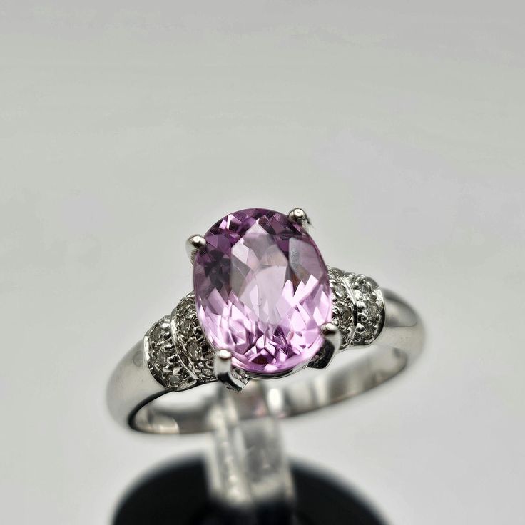 Indulge in the timeless allure of this vintage estate ring, crafted in luxurious 18k white gold. The focal point is a resplendent oval-cut kunzite, boasting a substantial 2.08 carats. Kunzite, known for its positive properties, brings a gentle, soothing energy and is often associated with matters of the heart. The captivating pink hue of the genuine kunzite is cradled in an elegant 4-prong setting, exuding a soft and romantic charm. Adorning the shoulders of the ring are genuine natural diamonds Oval Center Stone Gemstones For Formal Occasions, Oval Platinum Gemstone With Center Stone, Fine Jewelry Platinum Gemstones For Formal Occasions, Formal Platinum Gemstones Fine Jewelry, Formal Round Cut Platinum Gemstones, Luxury Gemstone With Center Stone For Anniversary, Luxury Platinum Gemstones With Accent Stones, Luxury Center Stone Gemstone For Anniversary, Elegant Oval Brilliant Cut Gemstones