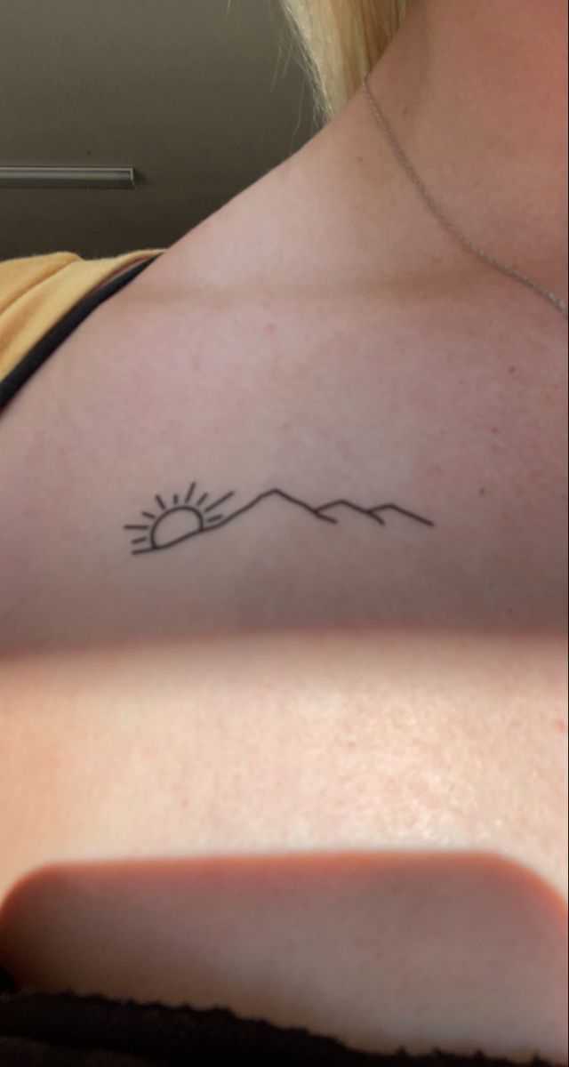 the back of a woman's shoulder with mountains and sun tattoo on her left arm