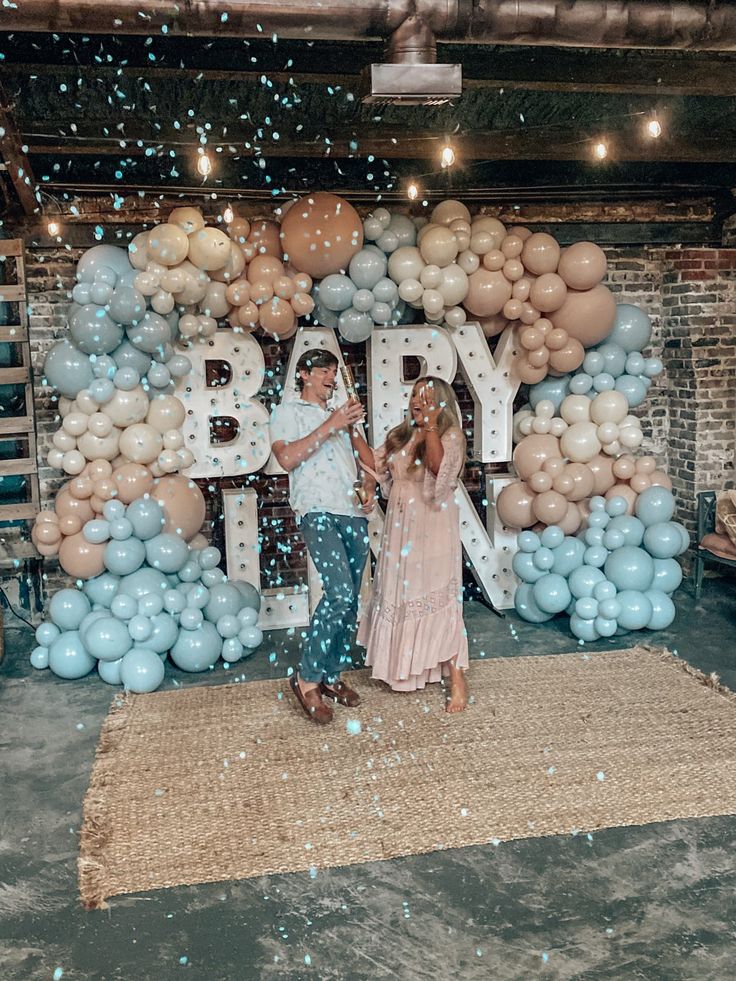 two people standing in front of a backdrop made out of balloons with the words baby on it