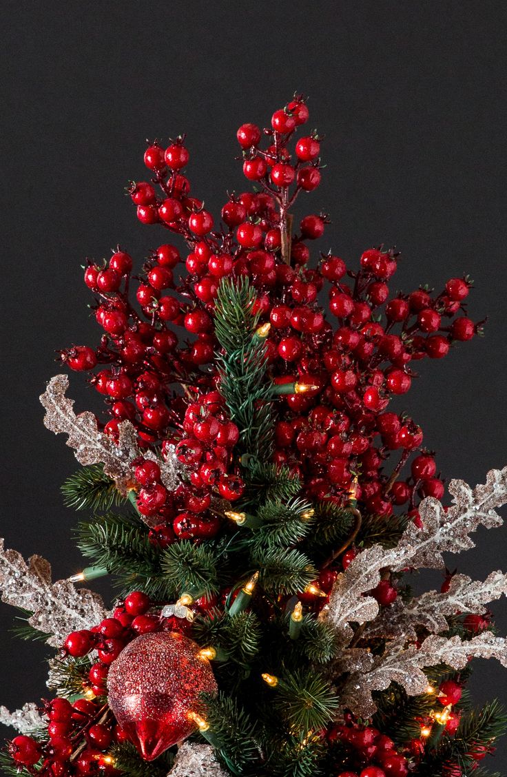 a small christmas tree with red berries and silver leaves in a vase on a table