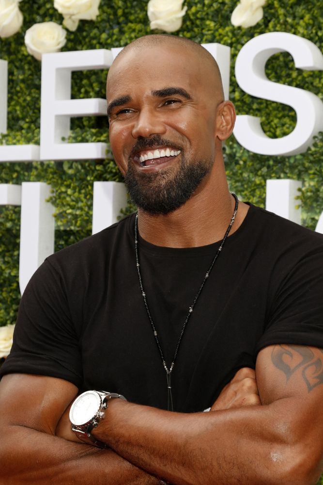 a smiling man with his arms crossed in front of a green wall and white roses