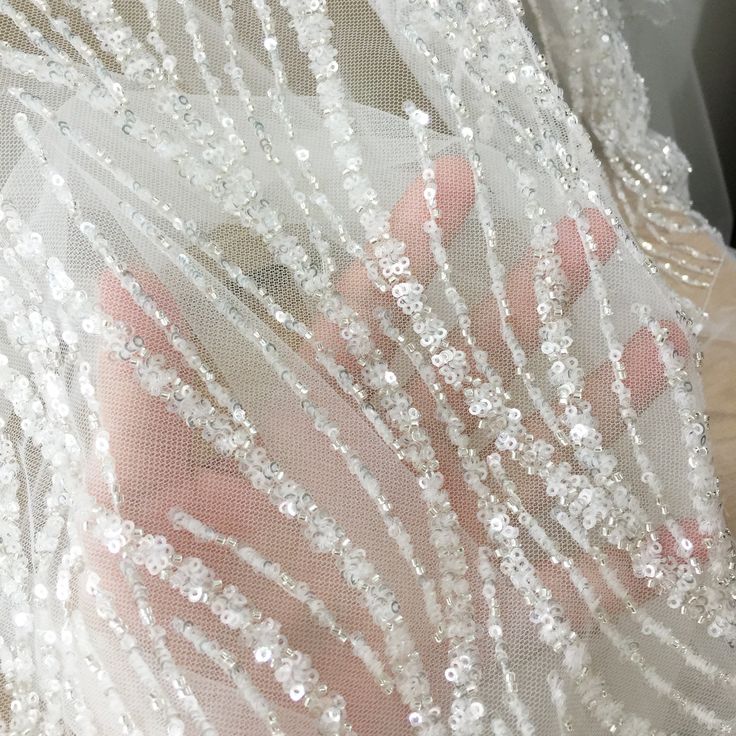 someone's hand is touching the sheer fabric on their wedding dress, which has sequins all over it