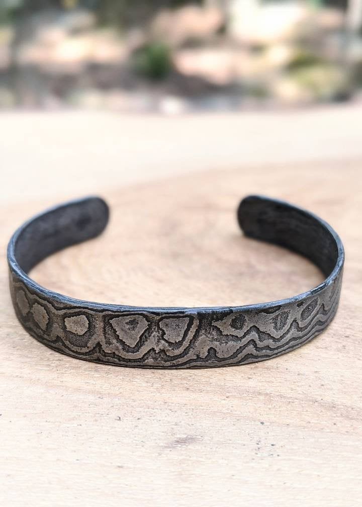 These bracelets are made to measures approximately 7 inches around and .5 inches in width. We are no longer taking custom orders for sizes at this time. Our damascus bracelets are hand forged from 1084 and 15n20. The damascus pattern varies with every bracelet; please expect that the one sent to you will be uniquely different in its own way. The photos show the general look of our hand-forged damascus. Each bracelet is coated with organic beeswax to protect it from the elements. As the wax coati Hand Cast Adjustable Bangle For Gift, Adjustable Hand Cast Bangle As Gift, Adjustable Hand Cast Bangle For Gift, Adjustable Oxidized Finish Cuff Bracelet As Gift, Adjustable Oxidized Cuff Bracelet, Mens Cuff Bracelets, Rustic Bracelet, Mens Cuff, 11th Anniversary