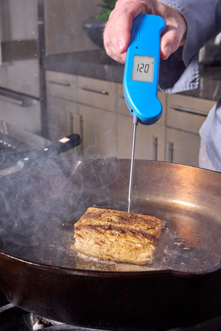 a person cooking food in a frying pan with a thermometer on it