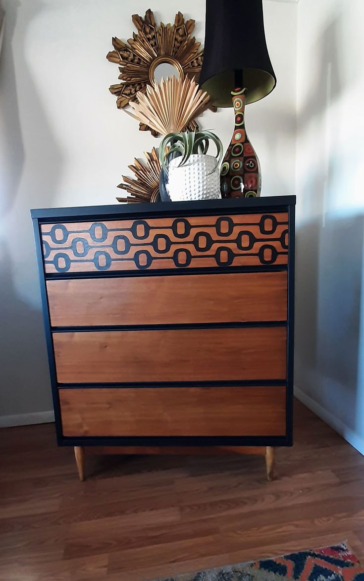 a wooden dresser sitting on top of a hard wood floor next to a lamp and vase