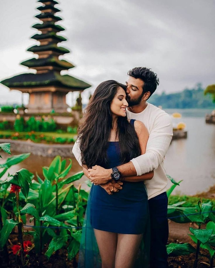 a man and woman standing next to each other in front of a body of water