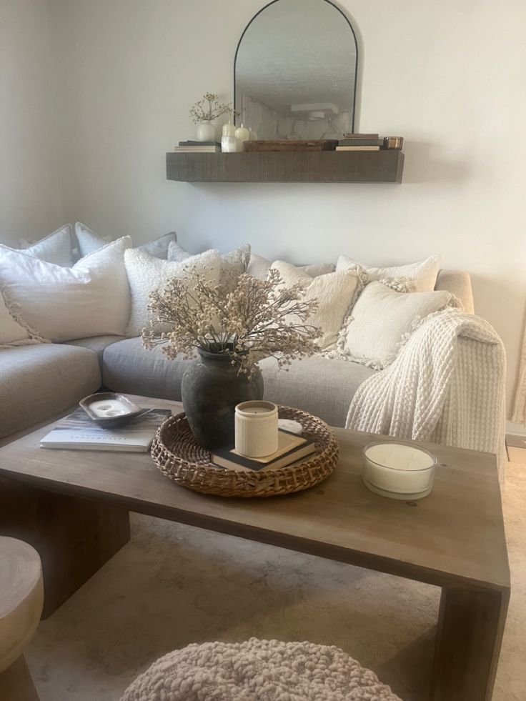 a living room with a gray couch and white pillows on the sofa, coffee table