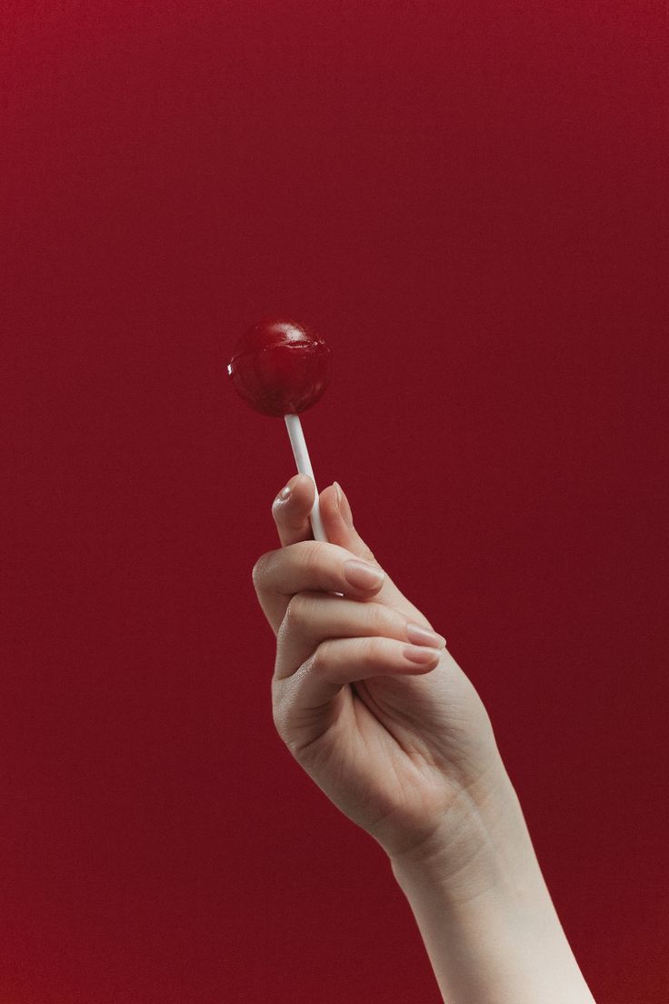 a hand holding a lollipop against a red background