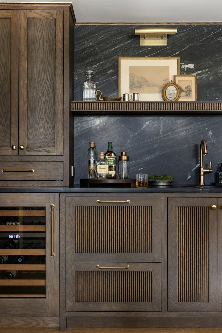 a kitchen with wooden cabinets and marble counter tops, along with wine bottles on the shelves