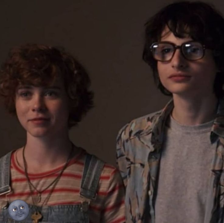 two young men standing next to each other in front of a wall and wearing glasses