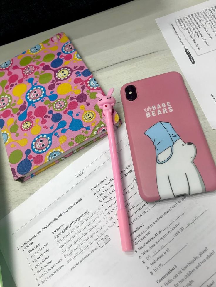 a pink phone case sitting on top of an open book next to a cellphone