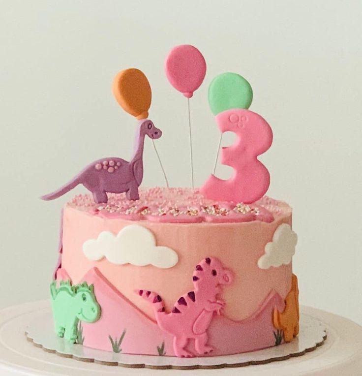 a birthday cake with pink and purple frosting, dinosaur balloons and stars on top