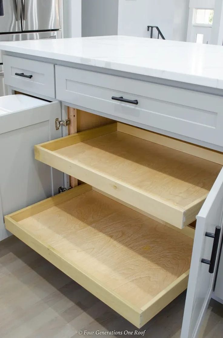 an open cabinet in a kitchen with white counter tops and drawers on the bottom shelf