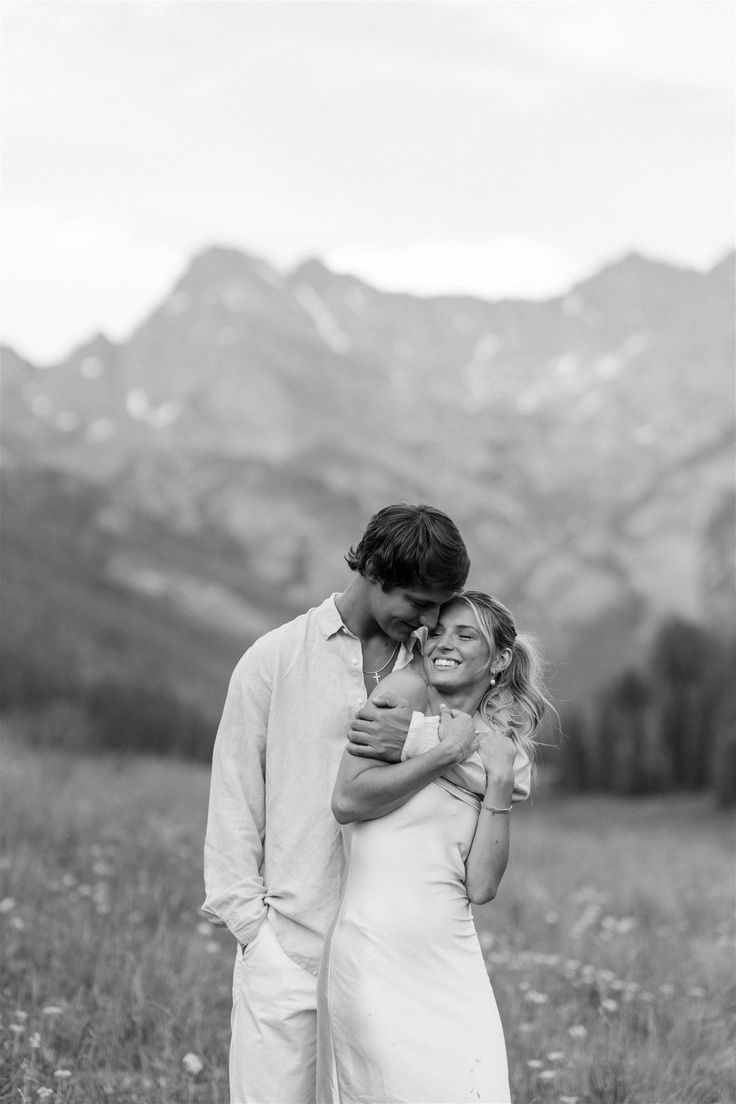 a man and woman standing in a field with mountains in the background