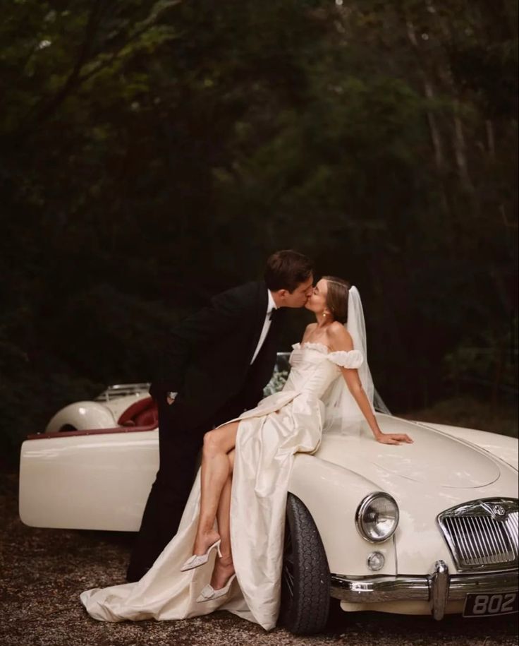 a bride and groom kissing in front of a vintage car