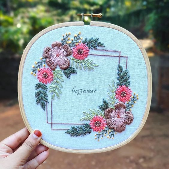 someone is holding up a cross stitch embroidery project with flowers and leaves in the center