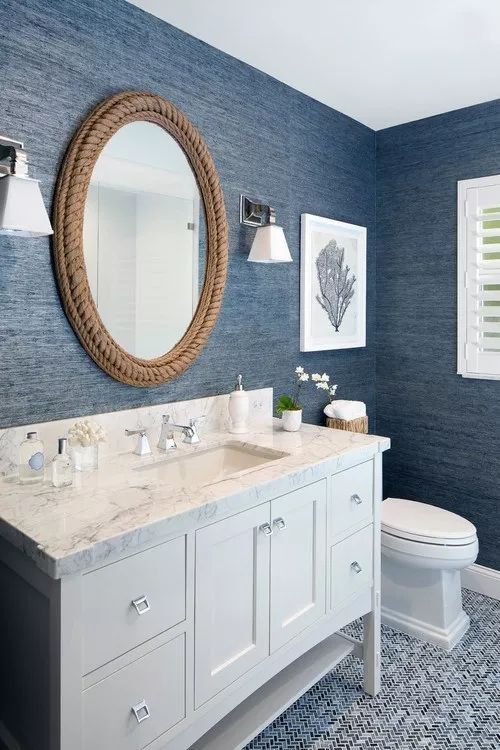 a bathroom with blue walls and white fixtures on the vanity, along with a round mirror