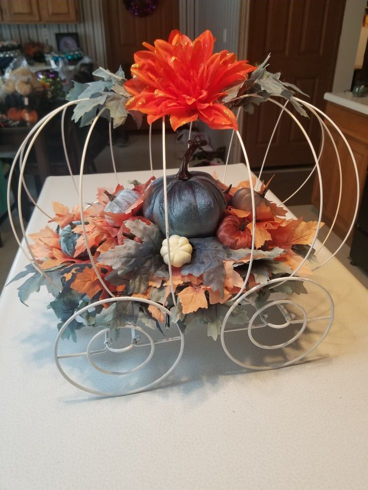 a pumpkin and some leaves in a wire basket on top of a white table cloth