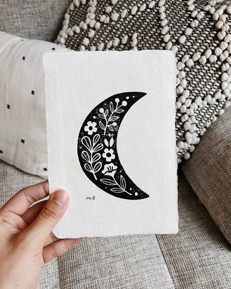 a hand holding up a piece of paper with the moon painted on it's side