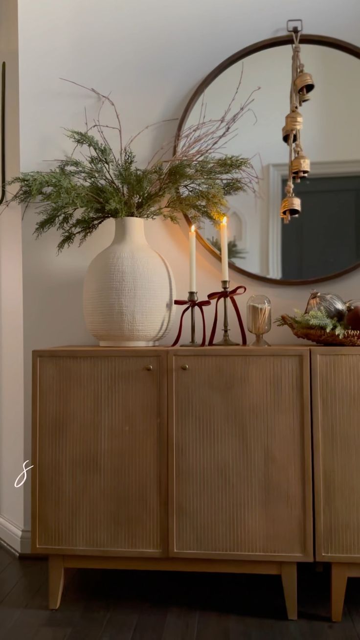 a white vase sitting on top of a wooden cabinet next to a mirror and candle