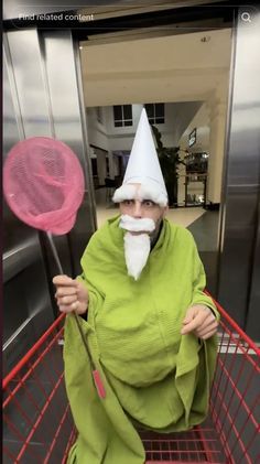 an old man in a green robe holding two pink lollipops while sitting in a shopping cart