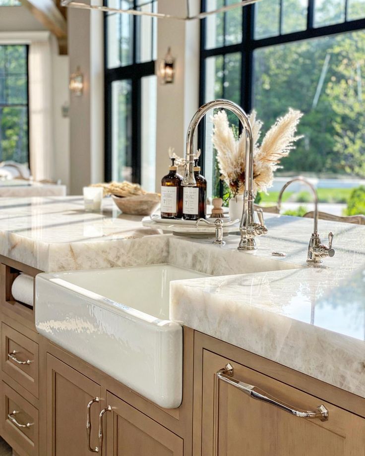 a large kitchen with marble counter tops and wooden cabinets in front of big windows that have lots of natural light coming through them