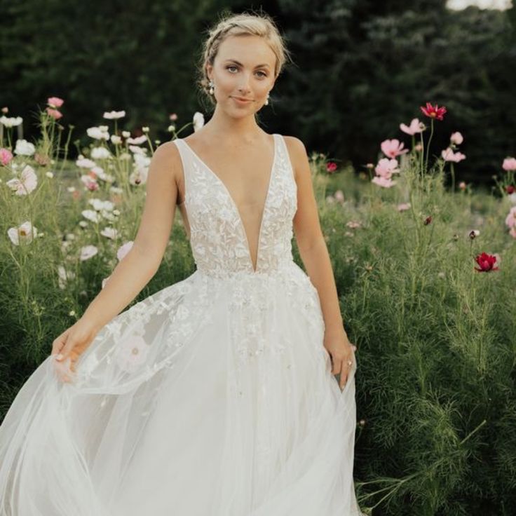 a woman in a white wedding dress standing in a field full of flowers with her hands on her hips