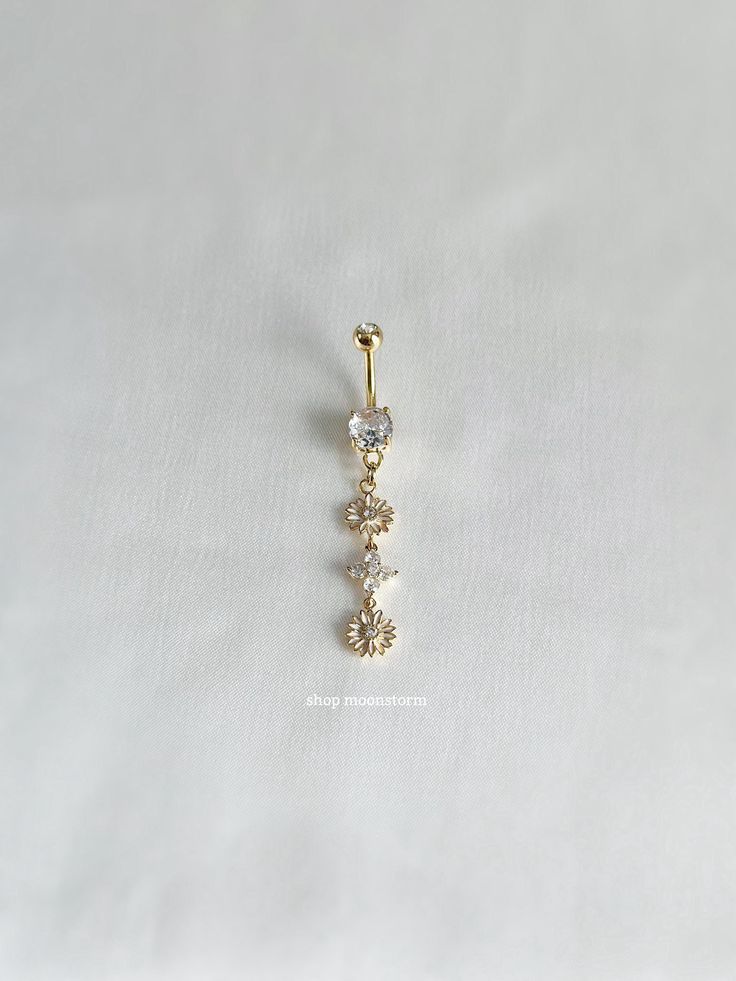 a gold nose piercing with three small flowers on it's end, sitting on a white surface