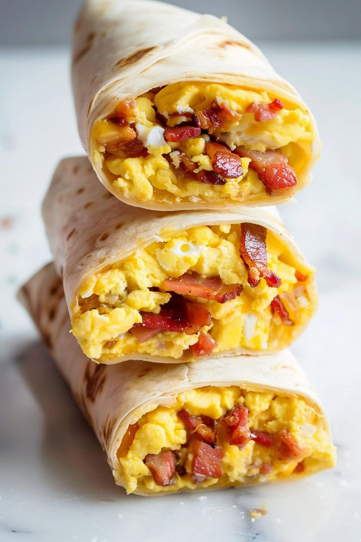 three breakfast burritos stacked on top of each other with scrambled eggs and bacon