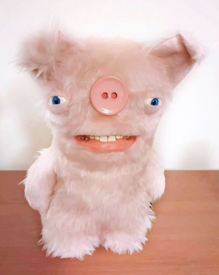 a white stuffed pig with blue eyes and a pink nose sitting on a wooden table