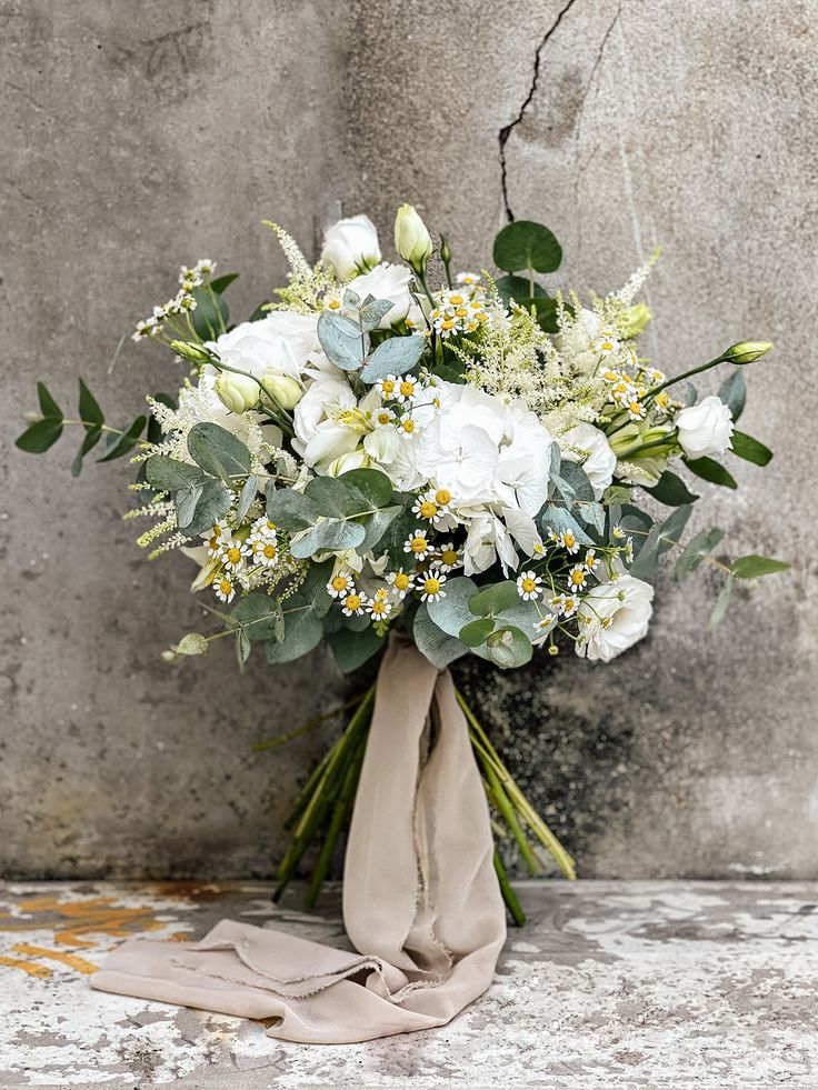 a bridal bouquet with white flowers and greenery on the side of a wall