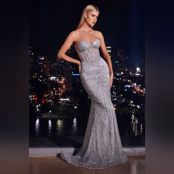 a woman in a silver dress standing on a balcony overlooking the city lights at night