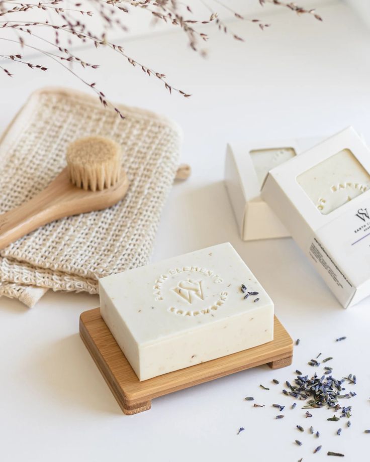 two soaps and a wooden brush on a white surface next to some lavender flowers