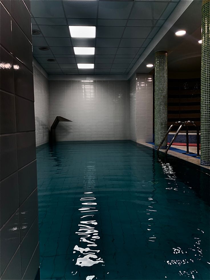 an empty swimming pool with blue water and tiled walls in the center, surrounded by green tiles