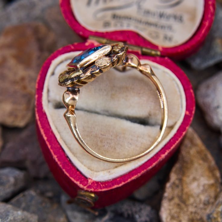 This lovely vintage ring features a lab created blue spinel in a full bezel setting that is decorated with a foliate motif halo. The ring is crafted in patinated 10k yellow gold and is currently a size 6.5. Vintage Cabochon Sapphire Ring For Wedding, Vintage 14k Gold Ring With Bezel Setting, Vintage Gold Sapphire Ring With Bezel Setting, Vintage 14k Gold Sapphire Ring With Bezel Setting, Vintage Blue Sapphire Ring With Bezel Setting, Victorian 14k Gold Jewelry With Bezel Setting, Vintage Sapphire Ring With Bezel Setting In 14k Gold, Art Nouveau Yellow Gold Rings With Rose Cut Diamonds, Vintage Yellow Gold Rings With Bezel Setting