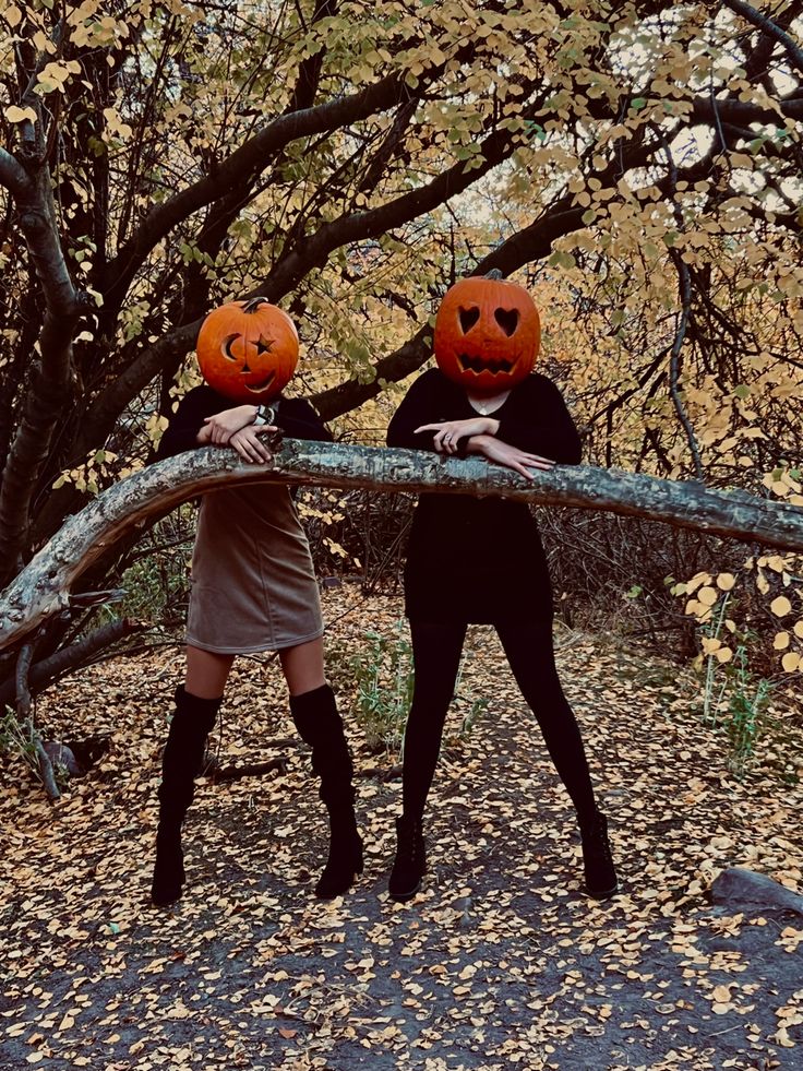 two women with pumpkin heads on their heads are holding a tree branch in the woods