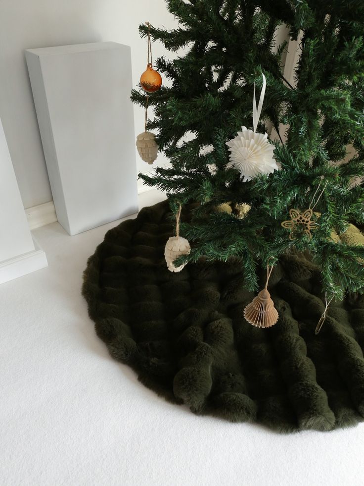 a christmas tree with ornaments hanging from it's branches and on the ground next to a white wall