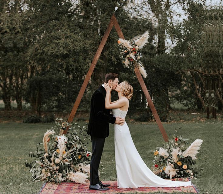 a bride and groom kissing in front of an outdoor ceremony arch with feathers on it