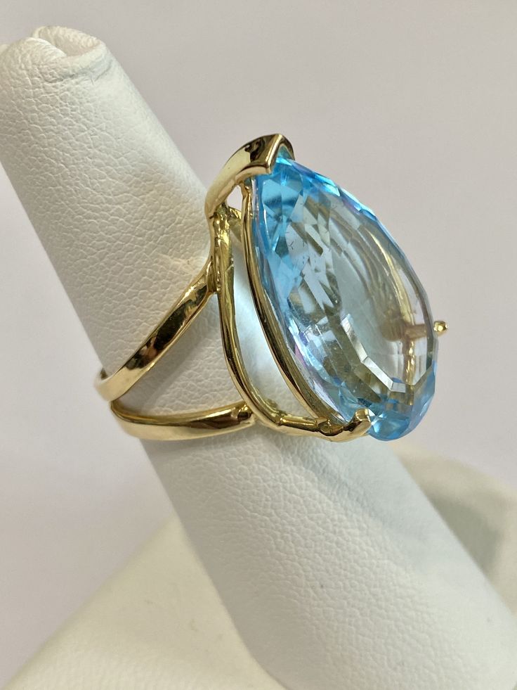 Stunning statement 14k yellow gold genuine blue topaz ring! This gorgeous ring contains a faceted pear cut genuine blue Topaz gemstone that weighs approximately 27.32 carats! The pear shaped gem is secured by 3 thick prongs. Incredible piece of fine jewelry featuring December birthstone! ERA - Modern, Estate METAL / MATERIAL - 14k yellow gold, 1 genuine Blue Topaz (approx. 27.32 cts) MARKINGS / HISTORY - Inside of ring is marked 14k CONDITION - Great vintage condition. SIZE / MEASUREMENTS - Size Fine Jewelry Yellow Gold Topaz Ring With Teardrop, Fine Jewelry Yellow Gold Topaz Teardrop Ring, Blue Topaz Teardrop Ring Fine Jewelry, Formal Yellow Gold Topaz Teardrop Ring, Formal Blue Pear-shaped Topaz Ring, Fine Jewelry Blue Pear-shaped Topaz Ring, Fine Blue Topaz Ring Pear-shaped, Formal Teardrop Blue Topaz Ring, Formal Pear-shaped Blue Topaz Ring