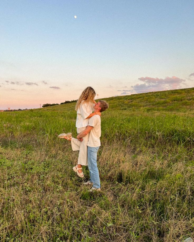 a man and woman hug in the middle of a grassy field at sunset with a full moon behind them