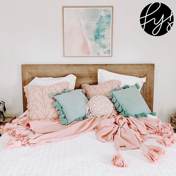 an unmade bed with pink and blue pillows on it in a white walled room