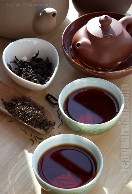 three tea cups filled with different types of tea on top of a wooden table next to pots and spoons