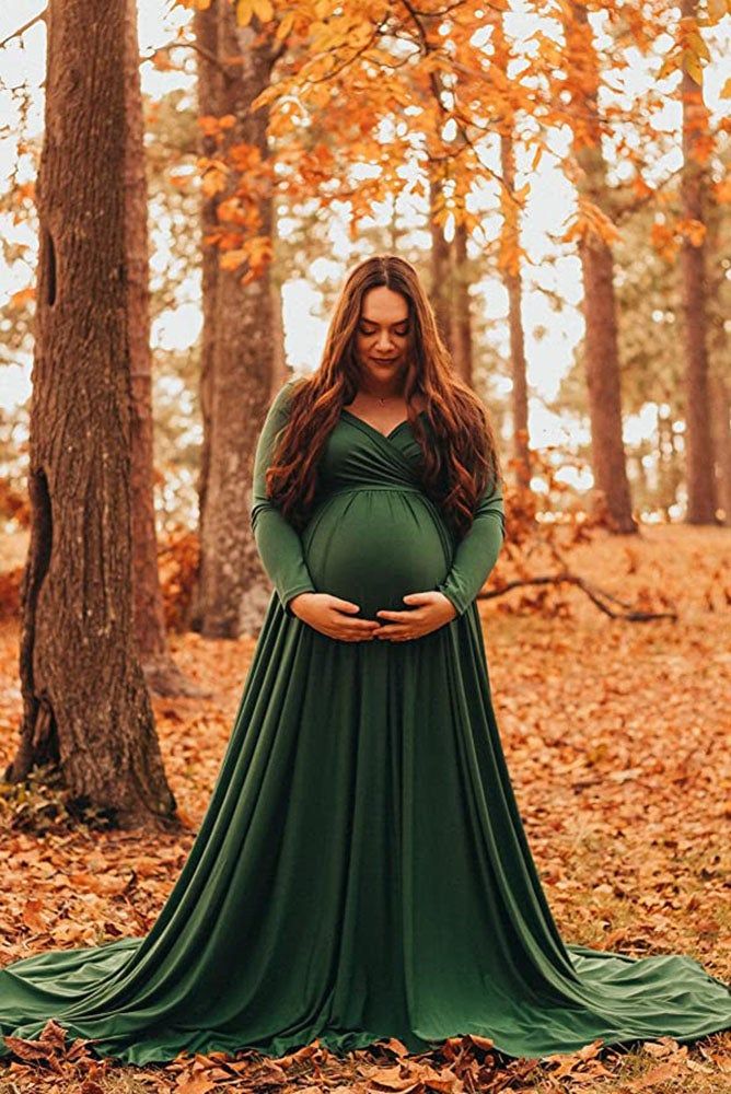 a pregnant woman wearing a green dress standing in the woods with her hands on her belly