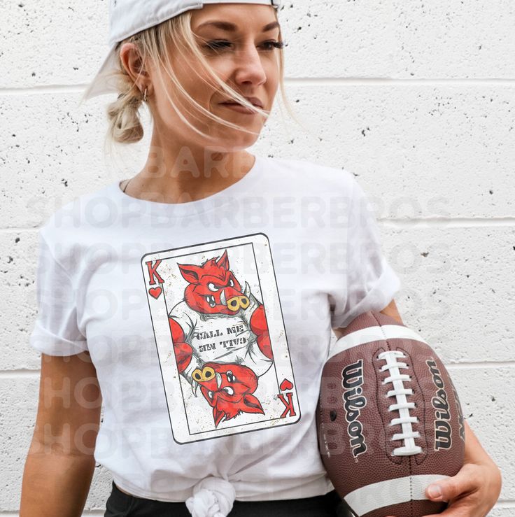 a woman is holding a football and wearing a t - shirt with an image of a devil on it