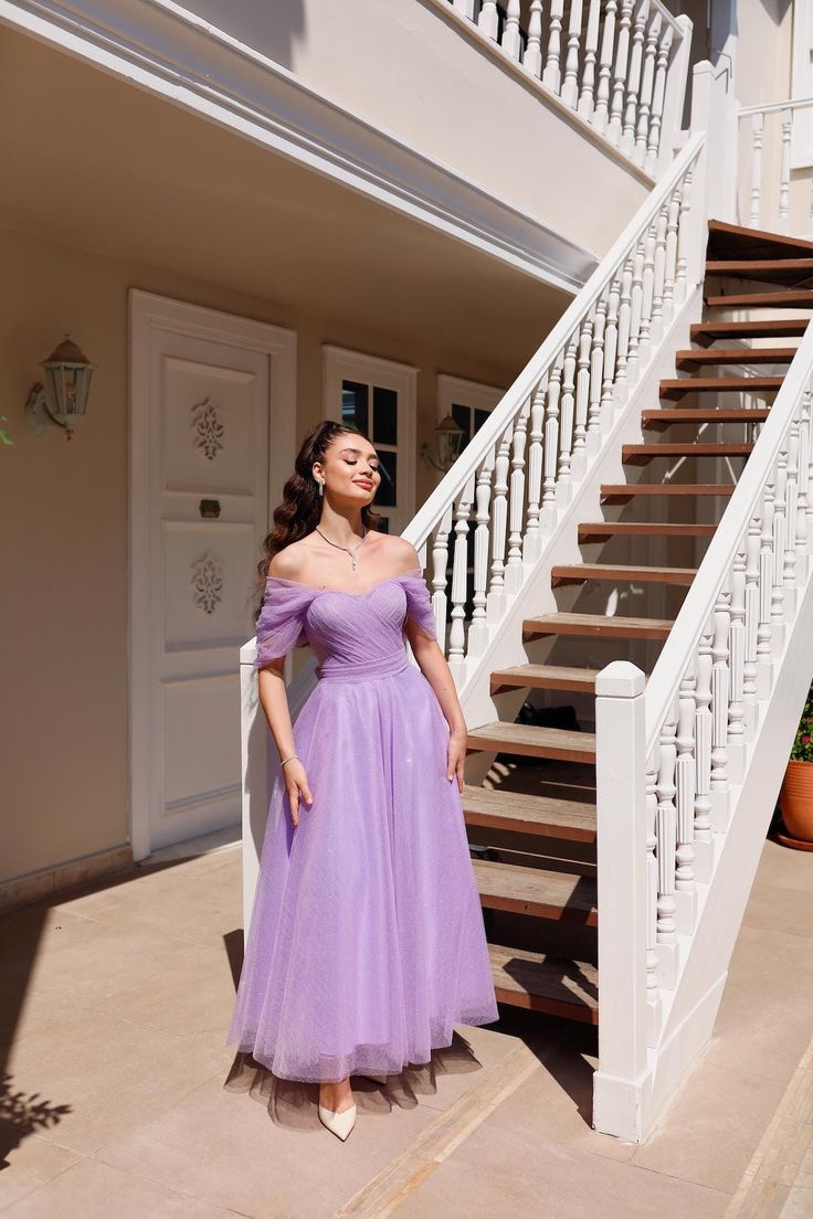 a woman standing in front of a staircase wearing a purple dress and white shoes with her hands on her hips