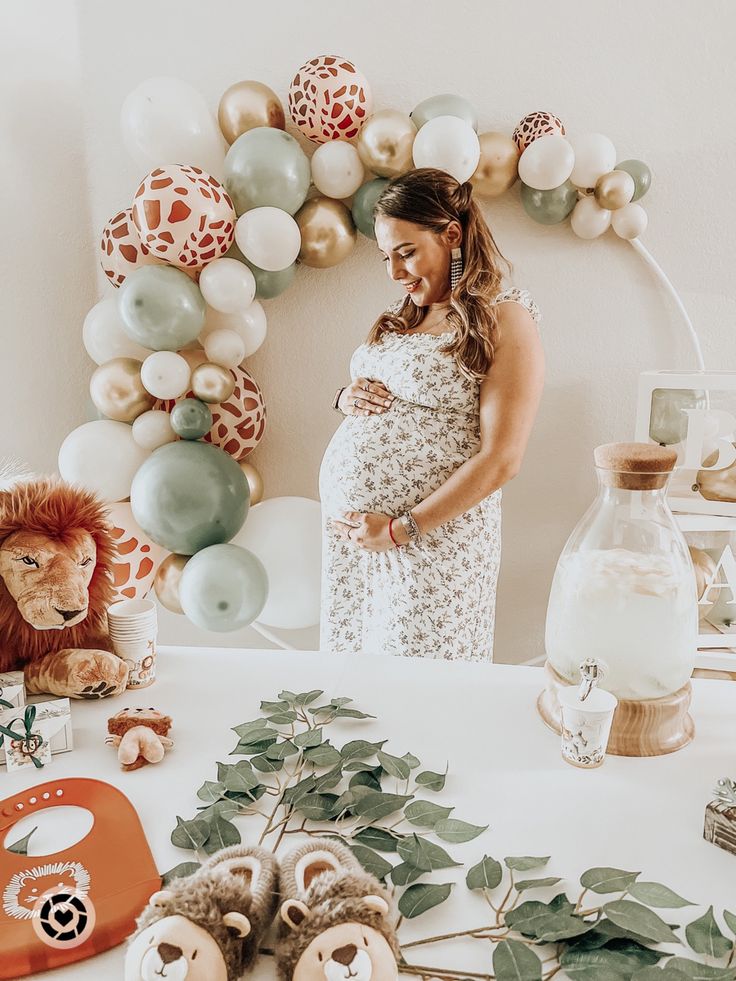 a pregnant woman standing in front of a table with balloons and stuffed animals on it